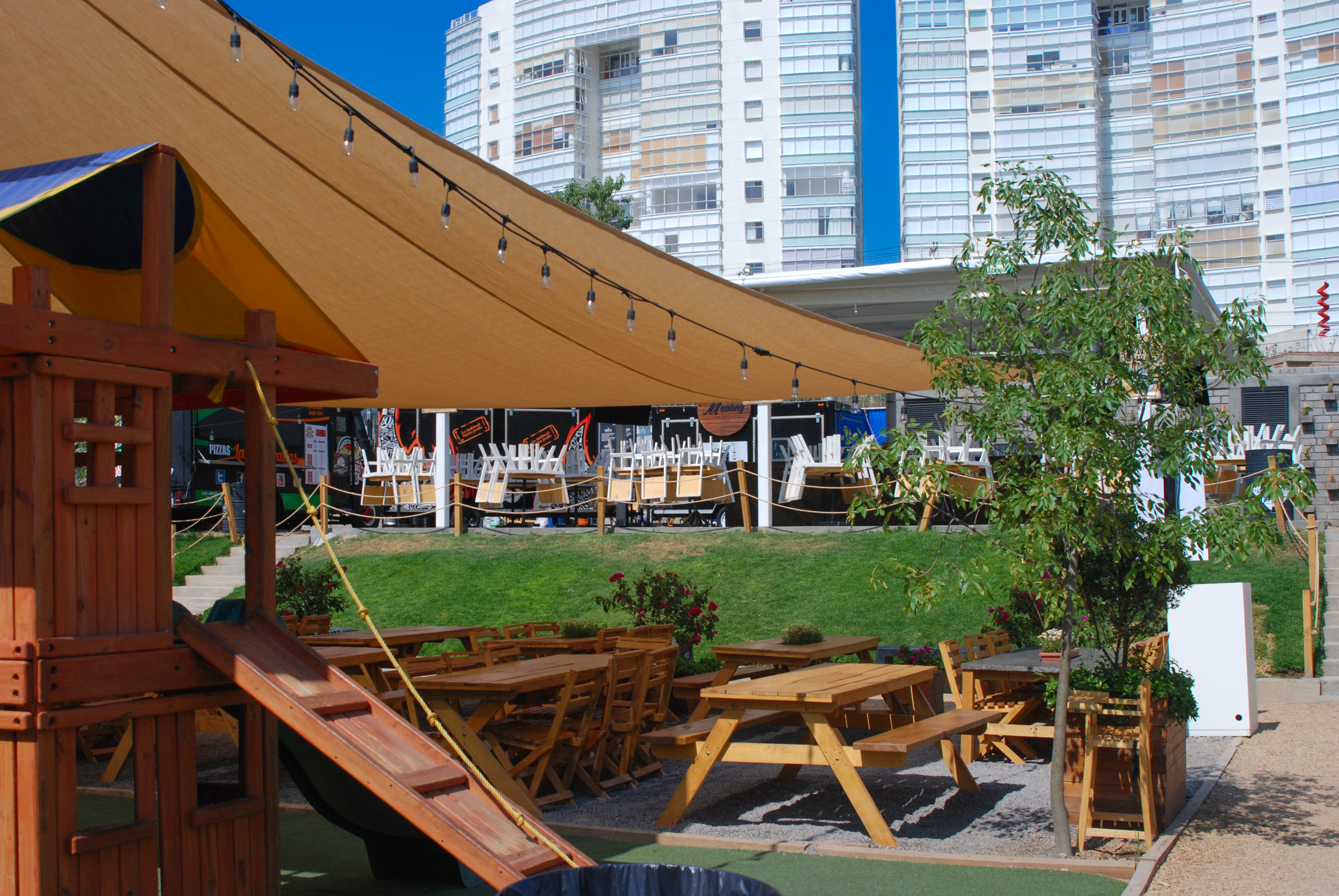 Zona de food trucks con techumbres tensadas de lona y mesas al aire libre, proyecto gastronómico Fer Et Ciment León